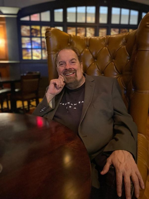Bob Sinkovic smiling in a leather wingback chair